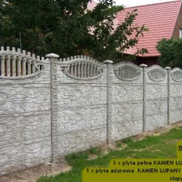 Długi, szary płot z prefabrykatów betonowych o fakturze łupanego kamienia, z ozdobnymi ażurowymi panelami w górnej części, oddzielający posesję z domem z czerwonym dachem od zielonego trawnika.