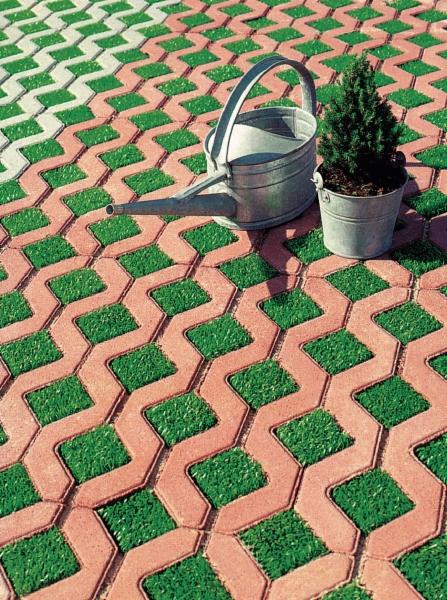 Ekologiczna nawierzchnia z czerwonej kostki ażurowej wypełnionej trawą, podlewana konewką. Mała choinka w doniczce stoi obok na kostce w Biłgoraju.