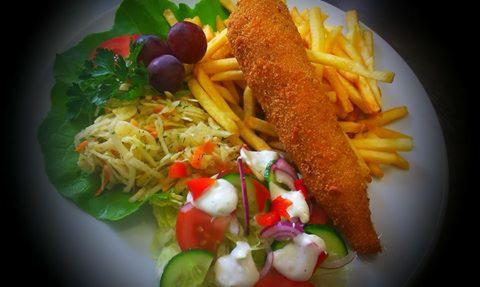 Kotlet w panierce, frytki i zestaw surówek na białym talerzu, dekoracja z winogron i natki pietruszki.