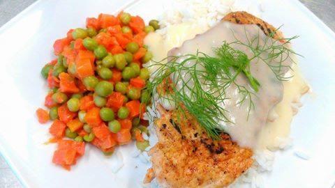 Danie na białym talerzu: smażona ryba z sosem, ryżem i warzywami (marchewka i groszek).