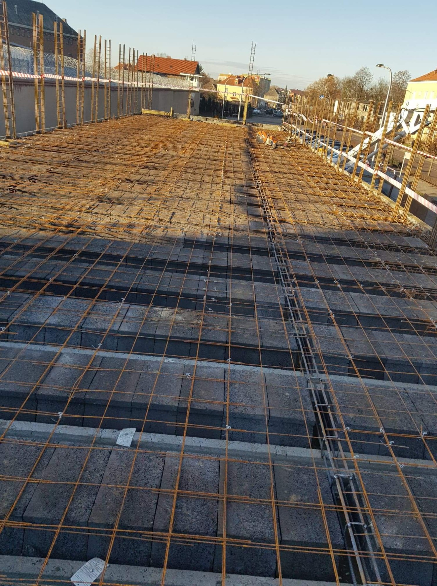 Zbrojenie fundamentów z użyciem stalowych prętów i bloczków betonowych, widok z góry na plac budowy w słoneczny dzień.