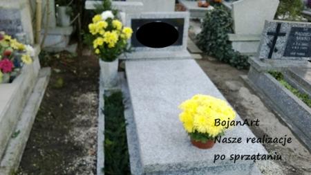 Wypielęgnowany nagrobek z jasnego kamienia, ozdobiony bukietem żółtych chryzantem w doniczce, otoczony zielenią, na tle innych nagrobków na cmentarzu.