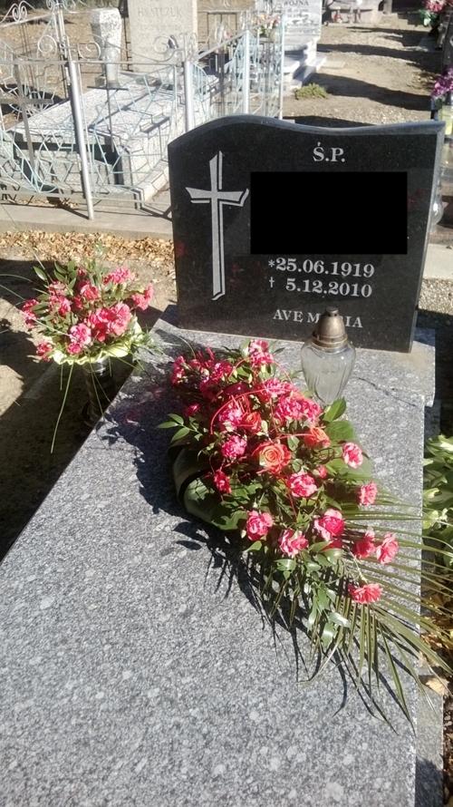 Granitowy nagrobek z datami i napisem 'Ave Maria', ozdobiony kompozycją z różowych róż i palmowych liści oraz szklanym lampionem.