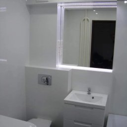 KABUD Kamil Karkowski - Biała łazienka z podświetlanym lustrem, umywalką z szafką i chromowanym przyciskiem spłuczki, widoczne odbicie w lustrze.