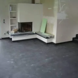 Ciemna, matowa wykładzina podłogowa w pokoju z kominkiem i ścianami w trakcie remontu, z zabezpieczonymi elementami mebli.