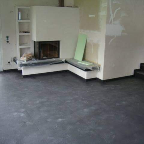 Ciemna, matowa wykładzina podłogowa w pokoju z kominkiem i ścianami w trakcie remontu, z zabezpieczonymi elementami mebli.