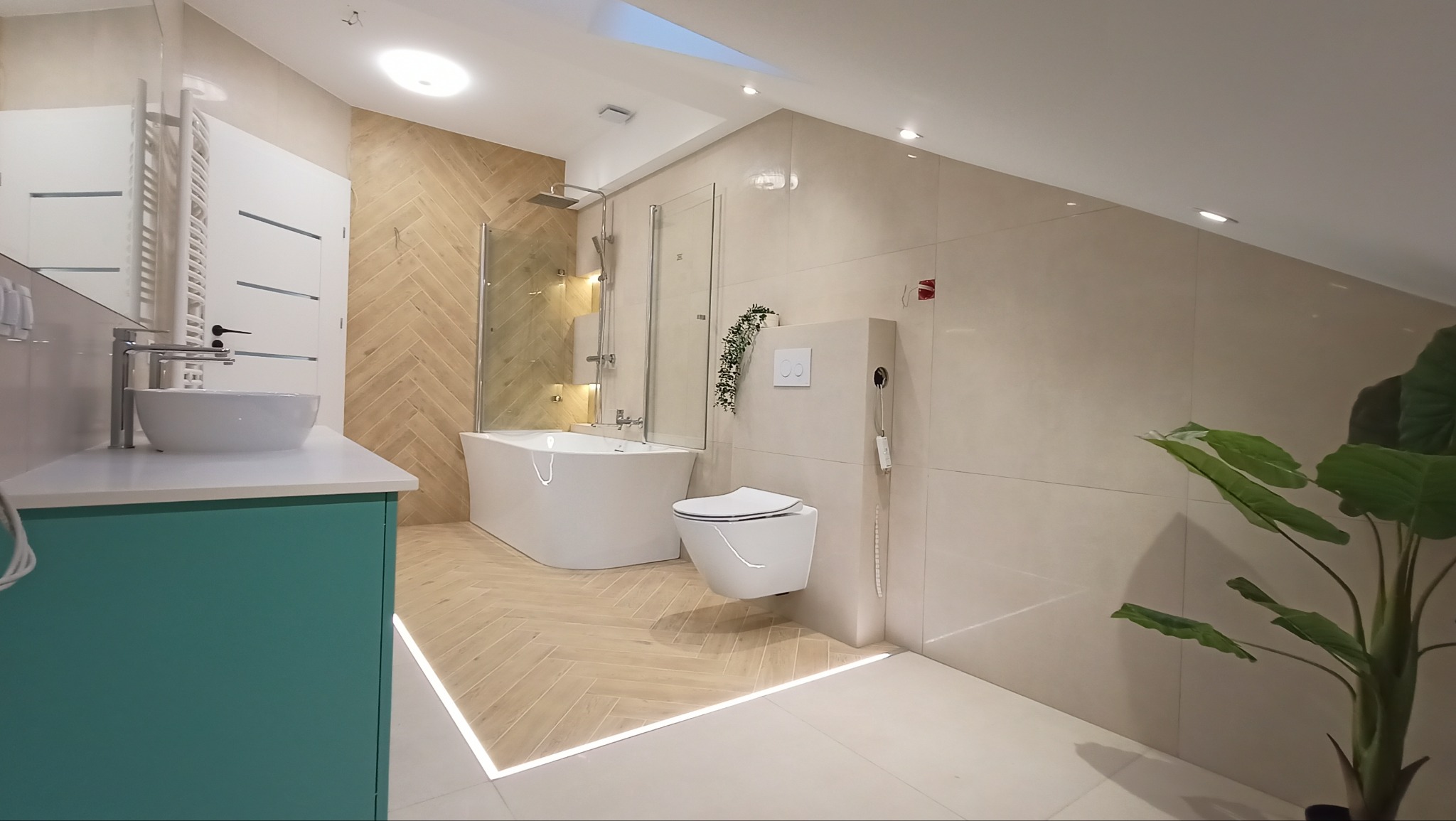 Nowoczesna łazienka na poddaszu z wanną wolnostojącą, podwieszaną toaletą, umywalką nablatową na turkusowej szafce i podświetleniem LED wzdłuż podłogi.