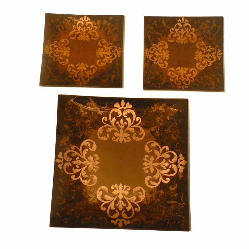 Trzy kwadratowe talerze dekoracyjne w odcieniach brązu z ornamentem roślinnym w kolorze złotym, ułożone w trójkąt na białym tle.
