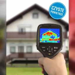 Kamera termowizyjna w dłoni, prezentująca rozkład temperatur na elewacji domu jednorodzinnego, wskazujący na potencjalne straty ciepła.