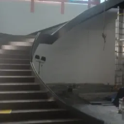 Wnętrze budynku w Bolesławcu w trakcie budowy, z widocznymi schodami metalowymi o zakrzywionej poręczy i elementami rusztowania w tle.