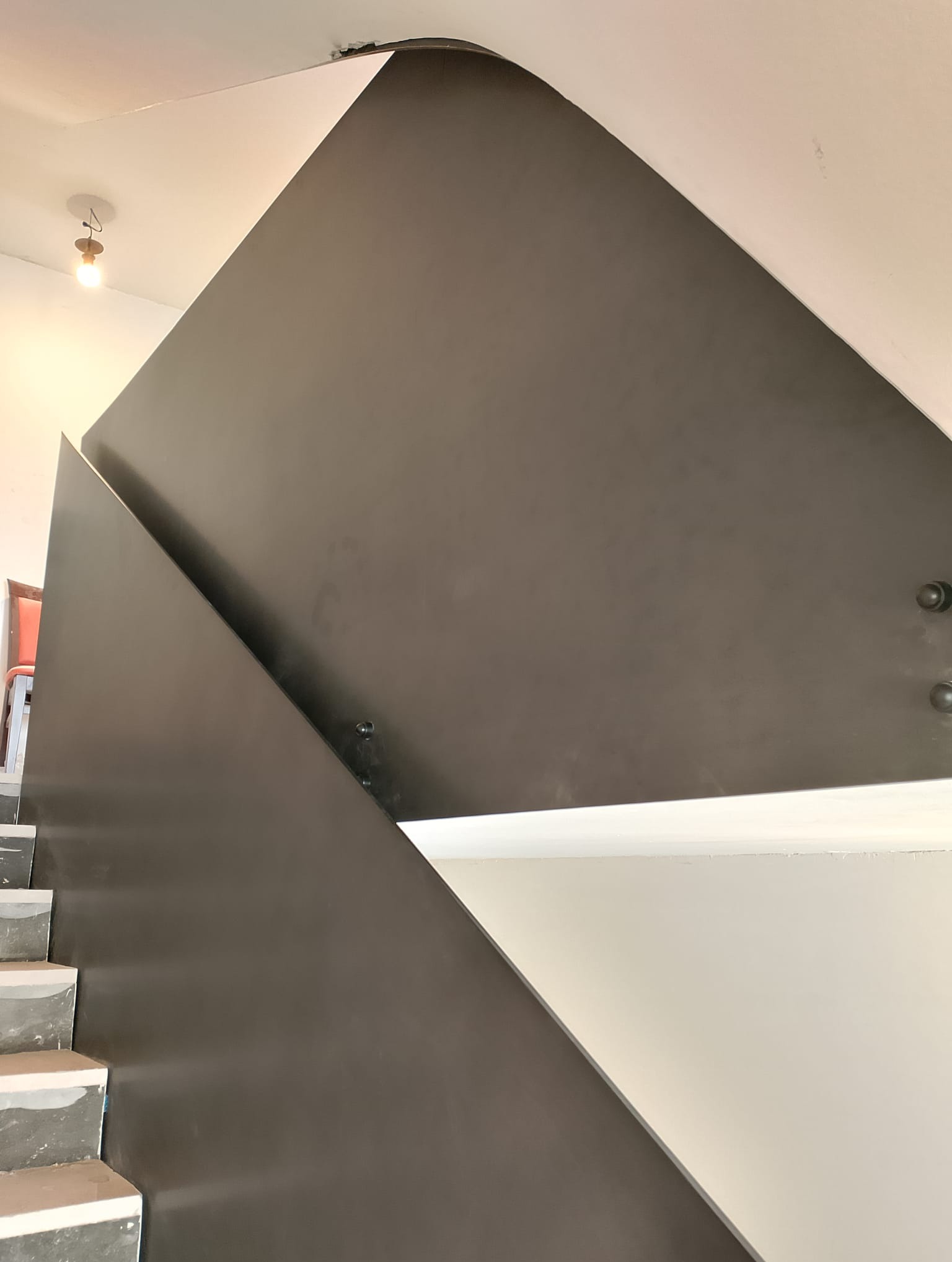 Nowoczesne schody metalowe z pełną, ciemnoszarą balustradą, mocowane na śruby, widok z dołu na fragment biegu schodów.