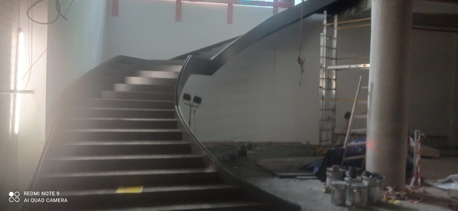 Wnętrze budynku w Bolesławcu w trakcie budowy, z widocznymi schodami metalowymi o zakrzywionej poręczy i elementami rusztowania w tle.