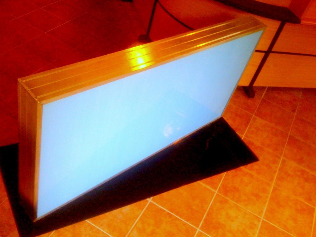 Podświetlany kaseton reklamowy o wymiarach 150x75 cm z metalową ramą, widoczny na pomarańczowej podłodze z płytek.