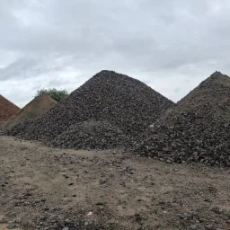 Góra ziemi, piasku i gruzu o różnej frakcji pod pochmurnym niebem. Na horyzoncie widoczny pomarańczowy element maszyny budowlanej.