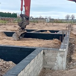 Firma-handlowo-usługow transportowa,,PE-TOM ''Krzysztof Pestka - Fundamenty budynku w trakcie budowy, zbrojenie i izolacja. Koparka z łyżką w tle, przygotowuje teren pod dalsze prace. Widok na plac budowy.