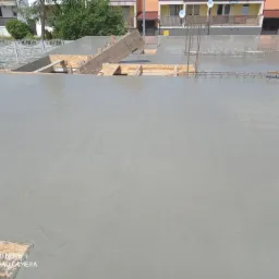 Świeżo wylana, gładka powierzchnia betonowa z widocznym zbrojeniem i deskowaniem, przygotowana do dalszych prac budowlanych, w tle budynki mieszkalne.