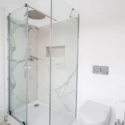 Nowoczesna kabina prysznicowa z deszczownicą i marmurowymi płytkami, widoczna toaleta wisząca i uchwyt na papier toaletowy w wykończonej łazience.