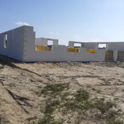 Wznoszone ściany parterowe budynku z bloczków Ytong na piaszczystym terenie, widoczne otwory okienne i palety z materiałem budowlanym w tle.