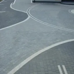 Wzorzysta nawierzchnia z kostki brukowej w odcieniach szarości, z białymi liniami oddzielającymi poszczególne strefy. Układanka tworzy estetyczny, nowoczesny design.