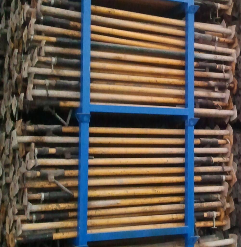 Sztaple metalowych stempli budowlanych, ułożonych warstwami w niebieskiej metalowej ramie transportowej. Widoczne ślady użytkowania.