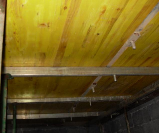 Żółte deski szalunkowe podtrzymywane metalowymi belkami tworzące system deskowania stropowego w trakcie budowy.