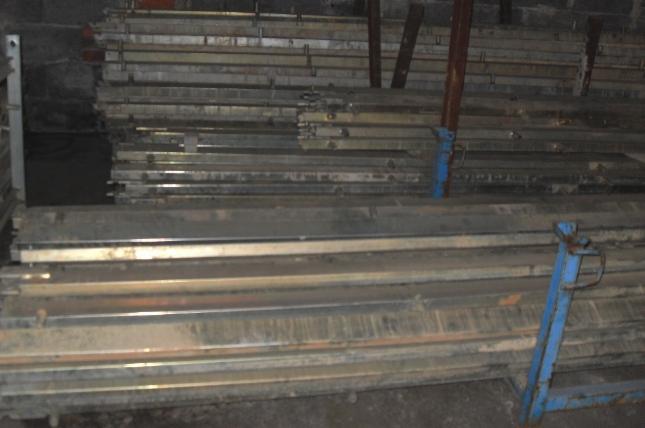 Stos metalowych szalunków stropowych składowanych w magazynie, widoczne ślady użytkowania i zabrudzenia.