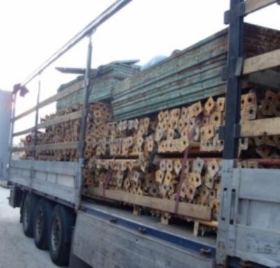 Ciężarówka załadowana kompletnymi szalunkami słupowymi, widoczne drewniane płyty i metalowe podpory z charakterystycznymi otworami, zabezpieczone czerwonymi pasami.