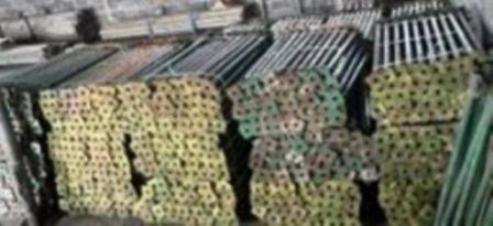 Stos metalowych stempli budowlanych o długości 4m, ułożonych w magazynie, widoczne także elementy szalunków.