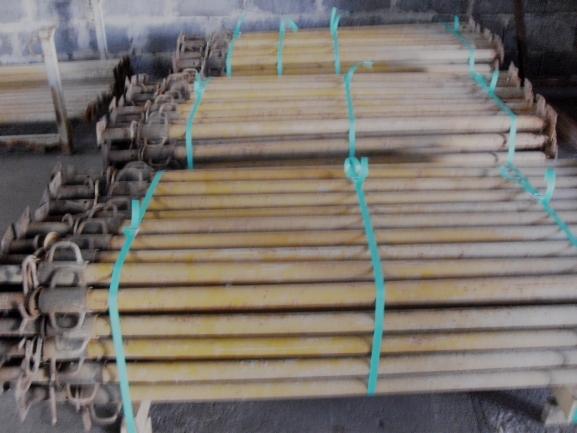 Stos belek podpierających, związanych niebieskim sznurkiem, składowanych w magazynie. Widoczne metalowe zakończenia belek.