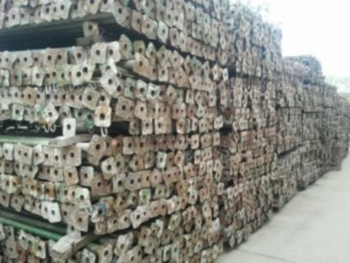 Stos metalowych stempli budowlanych o długości 4m, ułożonych poziomo w magazynie, widoczne kwadratowe podstawy z otworami.