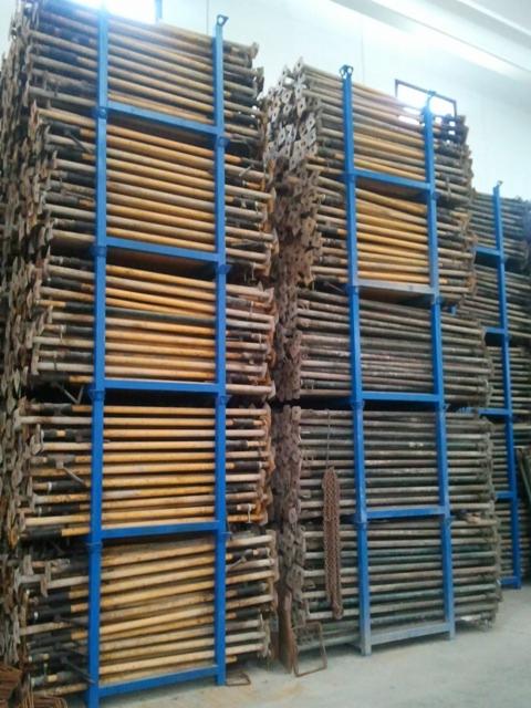 Magazynowane metalowe podpory budowlane w niebieskich stojakach, widoczne ślady użytkowania i rdzy.