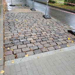 HALINA DANISZEWSKA BRUKARSTWO - Ułożona kostka granitowa w jesiennej scenerii, zabezpieczona barierkami. Widoczne liście na nawierzchni i mokra powierzchnia po deszczu. Kąt ujęcia z dołu.