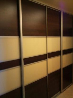 Czterodrzwiowa szafa przesuwna z panelami w kolorze kremowym i ciemnego drewna, z aluminiowymi prowadnicami, widoczna z boku.