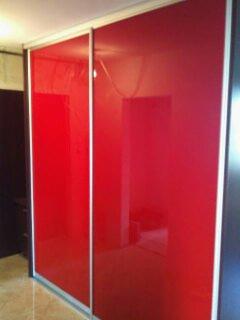 Czerwona szafa wnękowa z przesuwnymi drzwiami, wykonana na wymiar w Szczebrzeszynie. Widoczne srebrne obramowanie drzwi i intensywny, lustrzany połysk czerwonej powierzchni.