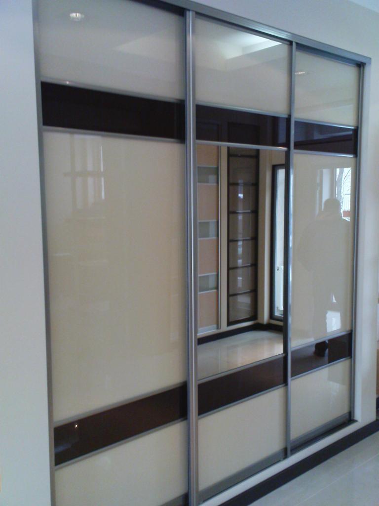 Trzydrzwiowa szafa przesuwna z beżowymi i brązowymi panelami, srebrne ramy, widoczne odbicie wnętrza z półkami.