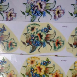 Arkusze kalkomanii z motywami kwiatowymi w różnych kolorach i stylach, częściowo odklejone od podłoża.