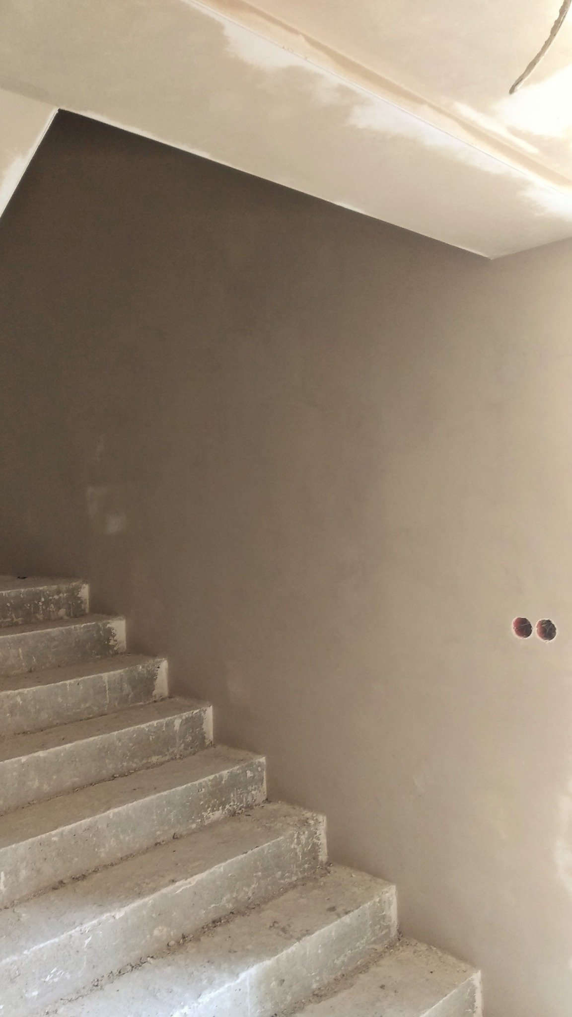 Świeżo otynkowana ściana przy betonowych schodach wewnętrznych, widoczne puszki elektryczne, surowy stan.