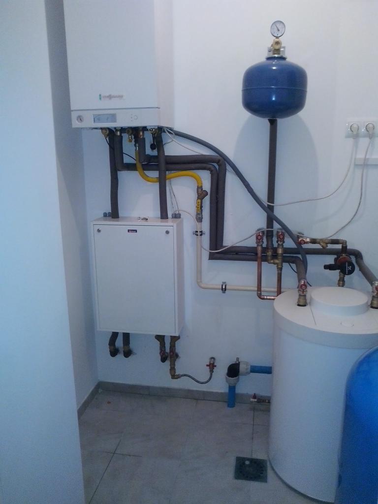 Kompaktowa kotłownia z białym piecem gazowym Viessmann, zasobnikiem ciepłej wody i niebieskim naczyniem przeponowym, widoczne rury miedziane i zawory