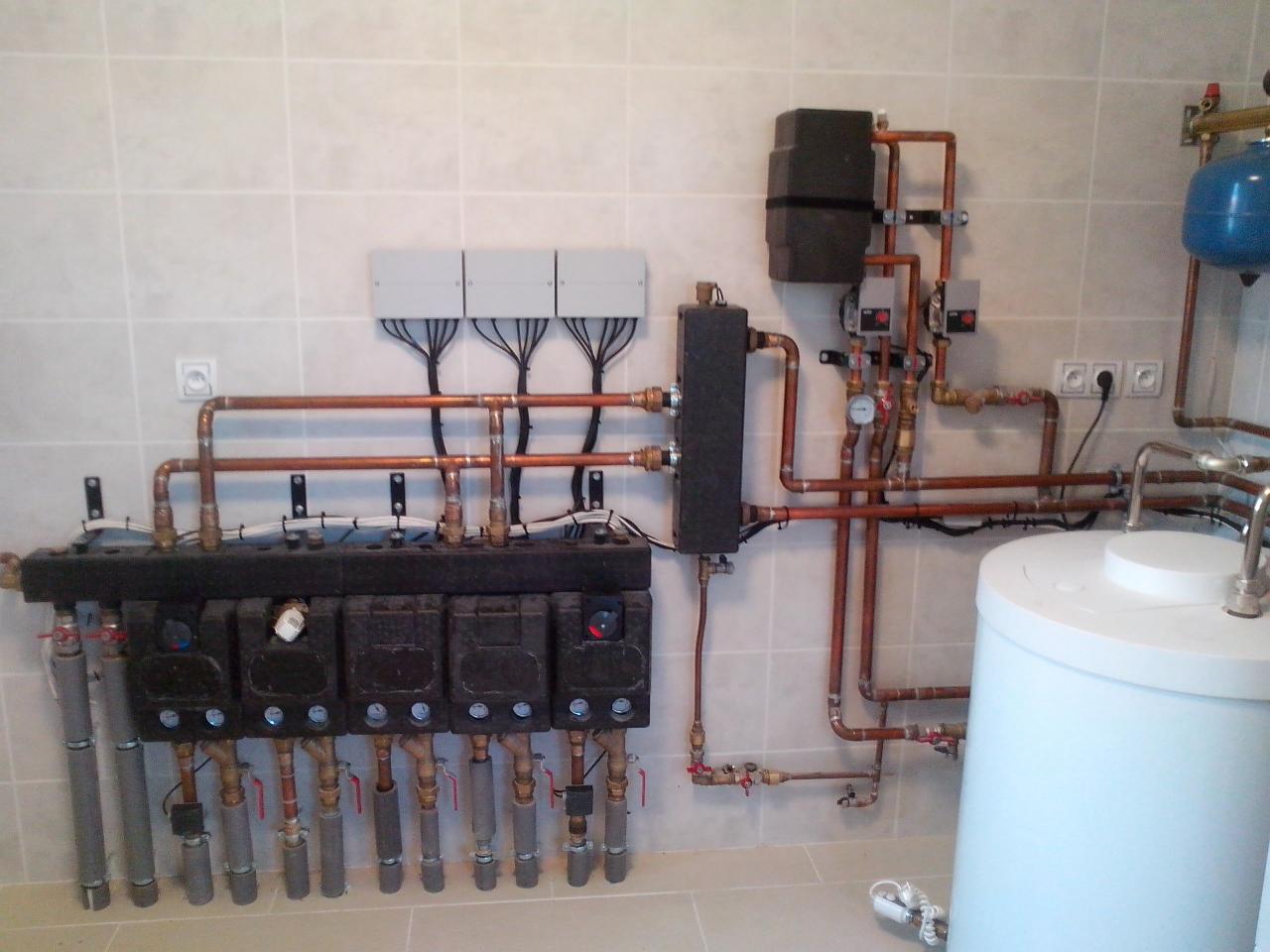 Rozbudowana instalacja centralnego ogrzewania z rozdzielaczem, pompami obiegowymi i zasobnikiem ciepłej wody użytkowej w kotłowni wyłożonej płytkami.