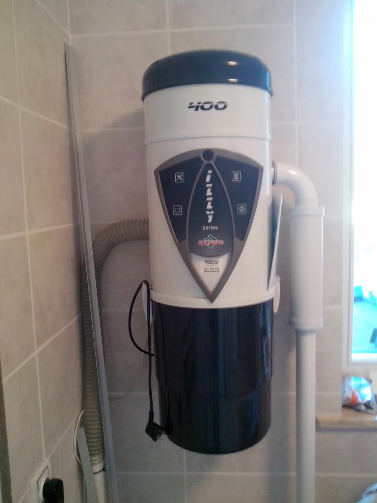 Centralny odkurzacz Illy 400 zamontowany na ścianie w łazience z szarymi płytkami, widoczne rury instalacyjne i wąż ssący.