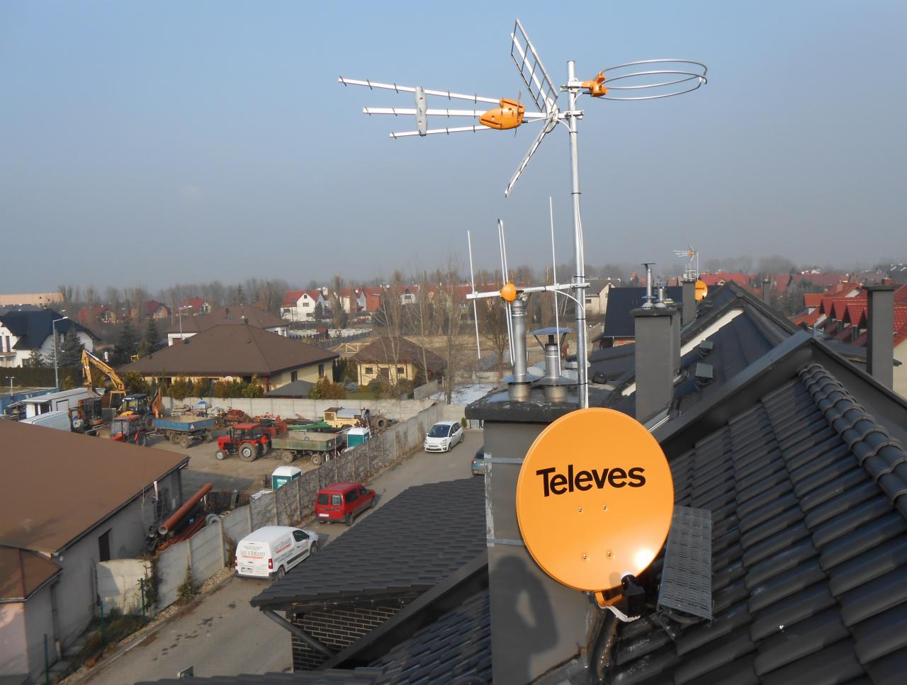 Antena satelitarna Televes i antena naziemna zamontowane na dachu domu jednorodzinnego z widokiem na okoliczną zabudowę i plac budowy.