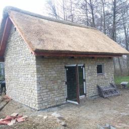 PHU KALBOT s.c. - Kamienny budynek gospodarczy z dachem krytym strzechą, widoczne detale konstrukcyjne i otoczenie budynku.