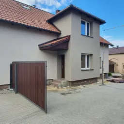 Dom jednorodzinny w Kamieńcu po świeżo wykonanym tynkowaniu elewacji, widoczne rusztowanie z boku budynku i otwierana brama wjazdowa.
