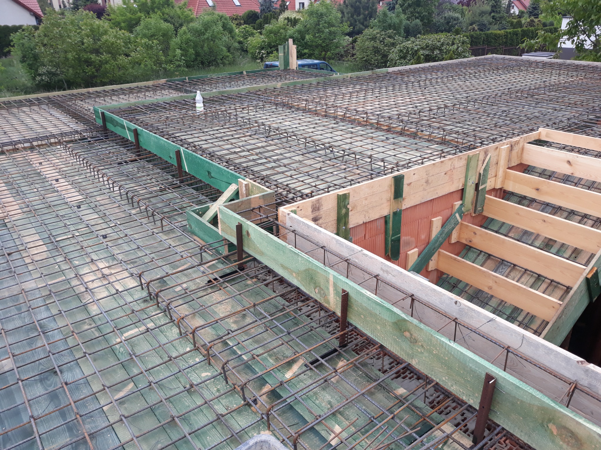 Zbrojenie stropu na drewnianym szalunku z widoczną butelką wody w tle, przygotowane do wylewania betonu.