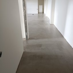 Rozbiórki i wyburzenia kompleksowo - Wnętrze biura w trakcie wykończenia: surowa podłoga, białe ściany, widoczne profile montażowe. Minimalistyczny design, jasne oświetlenie, perspektywa w głąb korytarza.