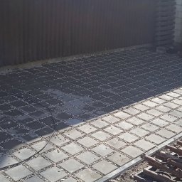 Rozbiórki i wyburzenia kompleksowo - Ułożona kostka brukowa z drobnymi kamieniami w przestrzeniach, tworząca wzór szachownicy. Widoczne narzędzia i fragment budynku w tle. Słoneczny dzień.