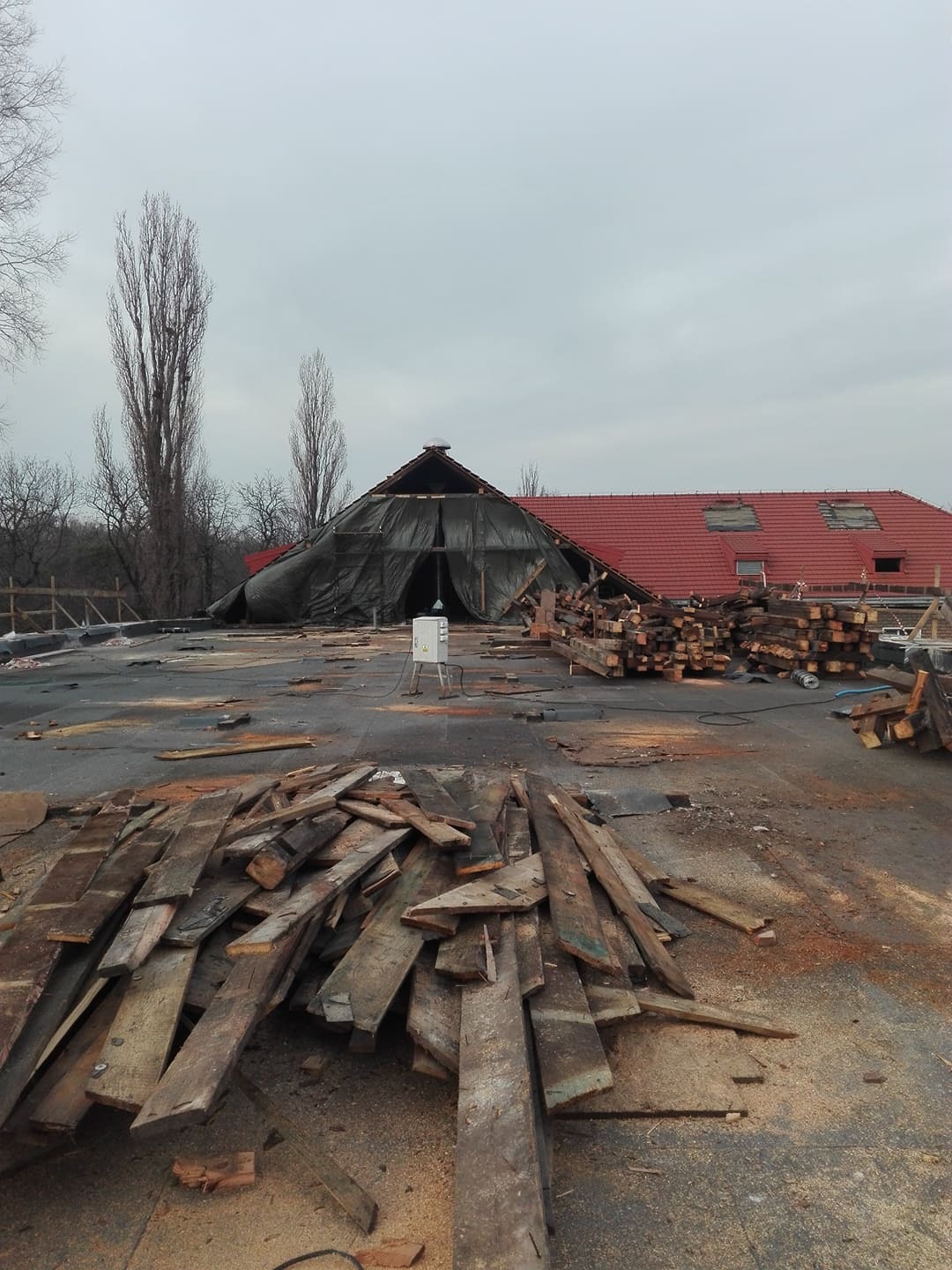 Demontaż dachu z widocznymi deskami, fragmentami pokrycia i zabezpieczeniem folią. Prace przygotowawcze do remontu dachu na tle pochmurnego nieba.