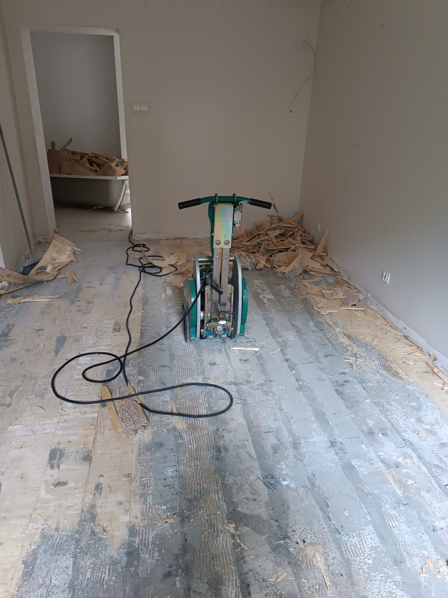 Cyklinowanie podłogi: szlifierka do parkietu w trakcie pracy, widoczne resztki starej powłoki i fragmenty odkurzone. W tle wanna z odpadami po renowacji.