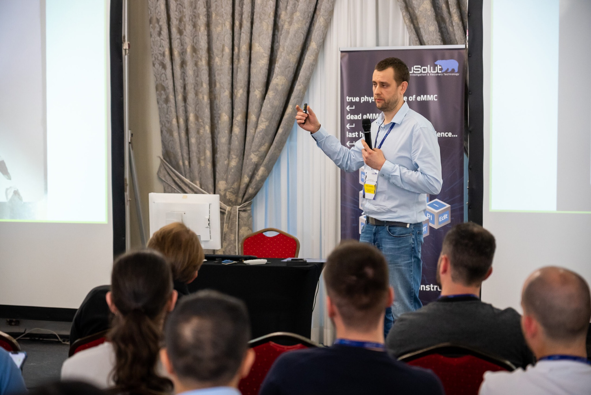 Prelegent z mikrofonem i pilotem prezentuje rozwiązanie dla eMMC podczas konferencji, widoczni słuchacze.