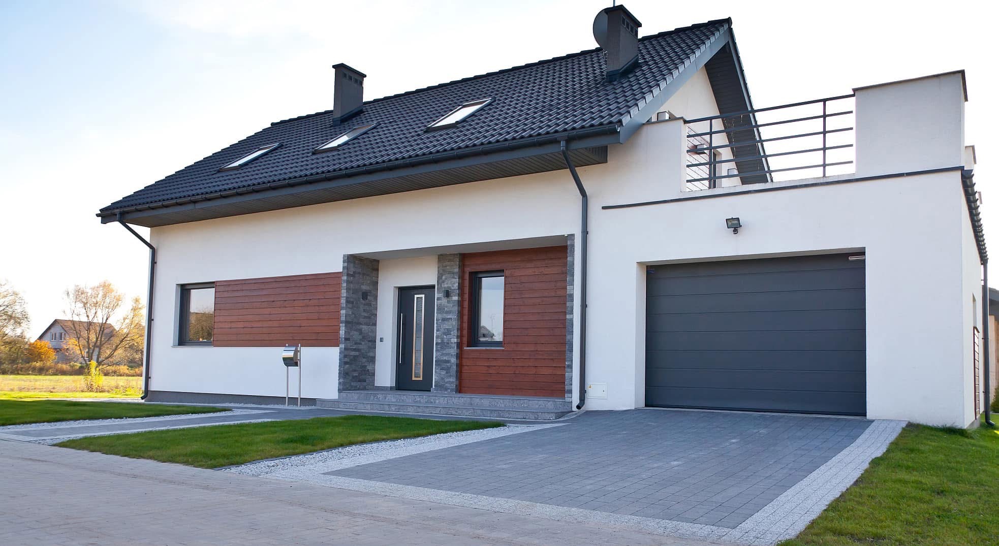 Nowoczesny dom jednorodzinny z szarą kostką brukową na podjeździe, widok z zewnątrz, jasna elewacja z elementami drewna i kamienia, garaż z automatyczną bramą.